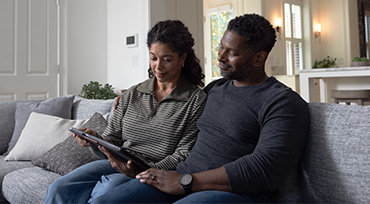 A couple sitting on a couch. The man has his laptop on his lap and the woman is looking at her mobile phone that has a background screen of a baby.